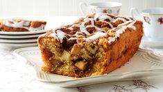 a piece of cinnamon apple coffee cake on a plate with two cups and saucers in the background