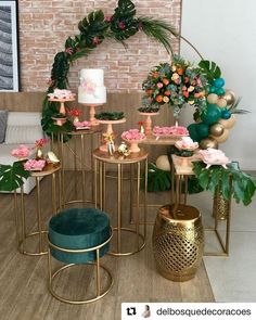 a table with cakes and flowers on it in front of a brick wall, surrounded by greenery