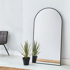 a mirror sitting on top of a wooden floor next to a chair and potted plant