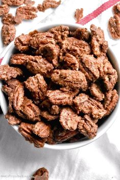 a white bowl filled with pecans on top of a white cloth next to a red and white striped napkin