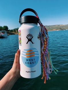 a hand holding a water bottle with the words west coast on it in front of a body of water