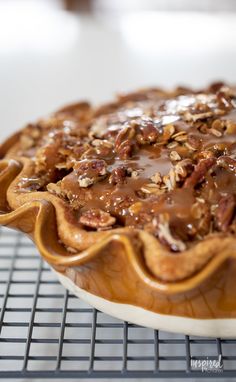 a pie sitting on top of a cooling rack covered in pecans and chocolate sauce