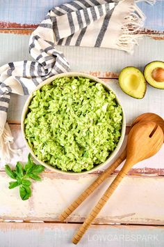 an avocado salad in a bowl with two wooden spoons next to it