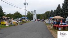 an outdoor flea market with tents and tables on the side of the road in front of trees