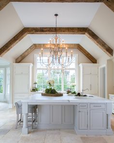 a large kitchen with an island and chandelier in the center, surrounded by white cabinets