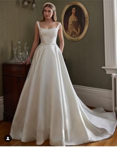 a woman in a white wedding dress standing next to a painting on the wall and looking at the camera