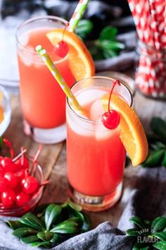 two glasses filled with orange juice and garnished with cherries on a table