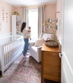 a woman holding a baby in her arms while standing next to a white crib