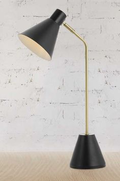 a black and gold lamp on a wooden table next to a white brick wall,