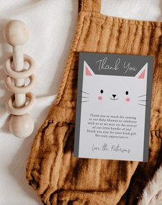 a thank card with a cat on it next to a wooden toy and some feathers