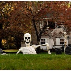 a skeleton sitting on the grass in front of a house with other halloween decorations around it