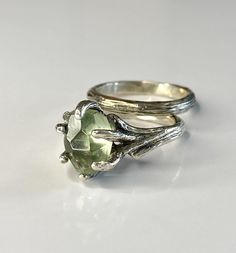 two silver rings sitting on top of each other with a green stone in the middle