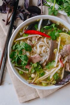 a bowl of soup with meat, noodles and cilantro on a napkin next to chopsticks