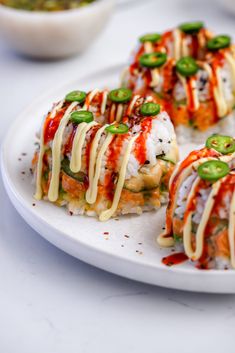 several pieces of sushi on a white plate with sauce and green peppers in the background