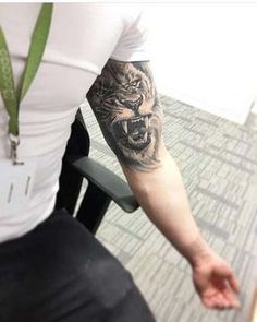 a man with a tiger tattoo on his arm sitting in front of a table and chair