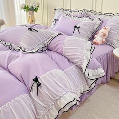 a bed with purple sheets and black ruffles on the bottom, along with a pink teddy bear