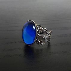 This ornate ring features a Sapphire blue cabochon (18 x 13 mm) on a stunning filigree band. The Sterling silver plated filigree ring is adjustable so one size fits all. The Sapphire blue cabochon catches the light beautifully. Nickel and lead free. The Bella ring is available in Black Onyx, Ruby red and Sapphire blue. This Bella Sapphire blue filigree ring perfectly complements many of our chokers. ***********************************************************Gift wrappingAll jewellery is beautifu Gothic Adjustable Rings For Formal Occasion, Gothic Style Adjustable Rings For Formal Occasions, Adjustable Gothic Style Rings For Formal Occasions, Gothic Formal Adjustable Rings, Ornate Ring, Steampunk Rings, Gothic Ring, Victorian Steampunk, Magical Jewelry