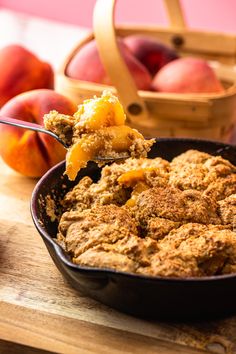 a close up of food in a pan on a table with peaches behind it