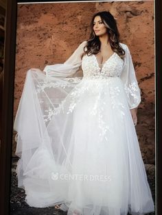 a woman in a white wedding dress standing next to a rock wall wearing a long veil