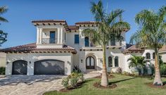 a large white house with palm trees in the front yard and two car garages