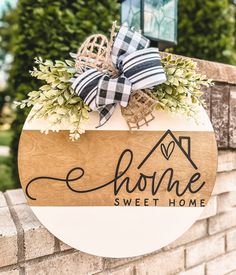 a wooden sign that says home sweet home on the side of a brick wall with a bow