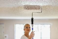 a woman holding a paint roller in her hand and looking up at the ceiling light