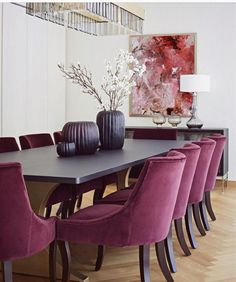 a dining room table with purple chairs and vases on top of it in front of a painting