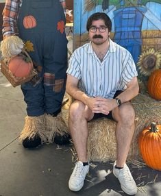 a man sitting on top of hay next to a scarecrow