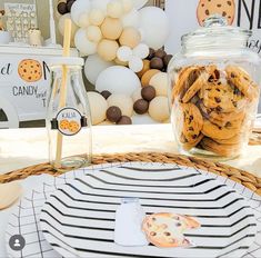 cookies in a glass jar sitting on a table next to a bottle of milk and some balloons