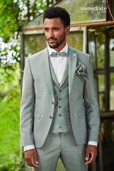 a man in a gray suit and bow tie posing for a photo with his hands in his pockets