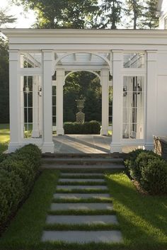 a white gazebo with steps leading to it in the middle of some grass and bushes