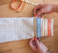 two hands are holding some fabric and gold chains on a wooden table next to scissors