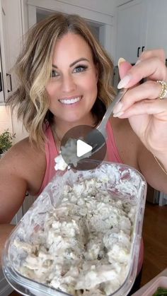 a woman holding a spoon over a container of food