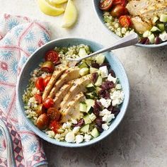 two blue bowls filled with chicken, rice and veggies next to lemon wedges