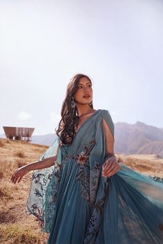 a woman standing on top of a grass covered hillside wearing a blue dress with flowers