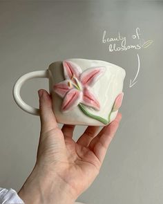 a hand holding a white coffee cup with pink flowers on it