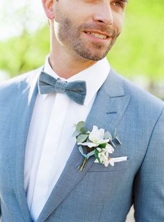 a man in a blue suit and bow tie smiles at the camera while wearing a boutonniere