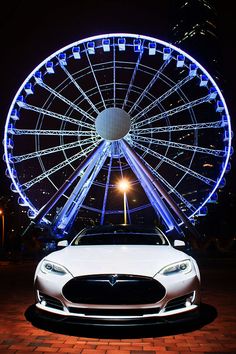 a white car parked in front of a ferris wheel at night with lights on it