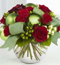 a vase filled with red roses and green christmas ornaments on top of a white table