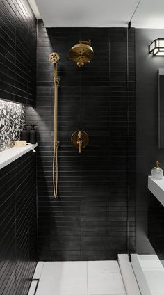 a black tiled bathroom with gold fixtures and white counter tops, along with a walk in shower