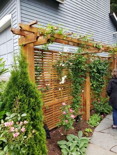 a woman standing in front of a wooden trellis with flowers growing on the side