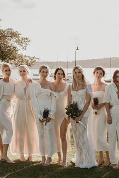 a group of women in white dresses standing next to each other on the grass near water