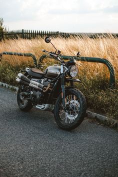 the motorcycle is parked on the side of the road next to tall grass and bushes