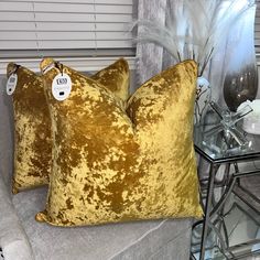 two yellow velvet pillows sitting on top of a couch next to a glass side table