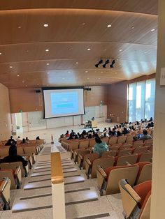 an auditorium with rows of chairs and people sitting in the seats watching a presentation on a projector screen