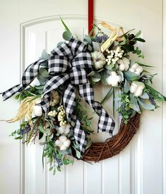 a wreath with white flowers and greenery hangs on the front door, decorated with black and white gingham ribbon