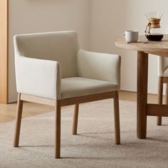 a white chair sitting on top of a rug next to a wooden table and coffee cup