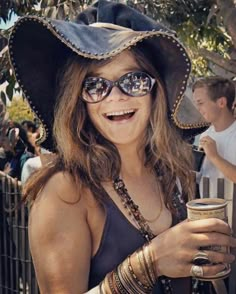 a woman wearing a pirate hat and sunglasses holding a drink in her hand while standing next to a fence