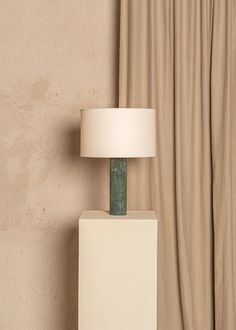 a lamp sitting on top of a white block next to a curtained window with drapes