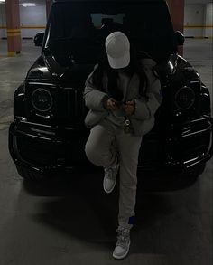 a woman sitting on the hood of a black car in a parking garage while looking at her cell phone